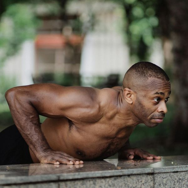 A man in a focused state, preparing for a bodyweight exercise, with clear muscle definition.